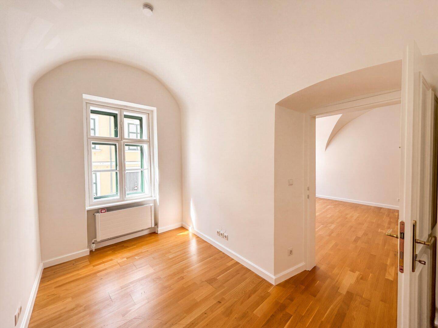 Gemütlicher Raum mit Gewölbedecke, Holzboden und einem Fenster, ideal als Schlaf- oder Arbeitszimmer.