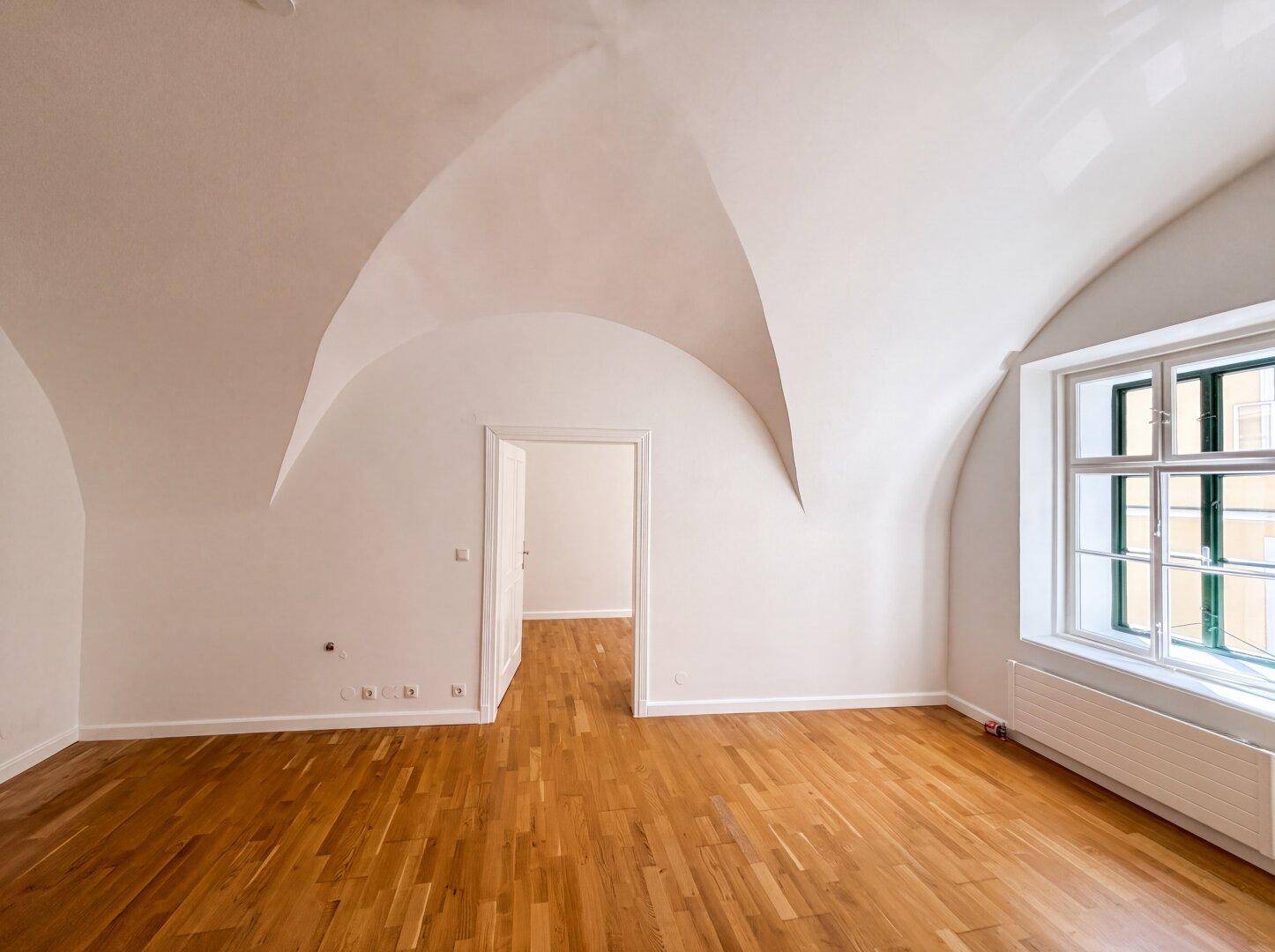 Geräumiger Raum mit eleganter Gewölbedecke und glänzendem Holzboden, bietet eine helle und offene Atmosphäre.