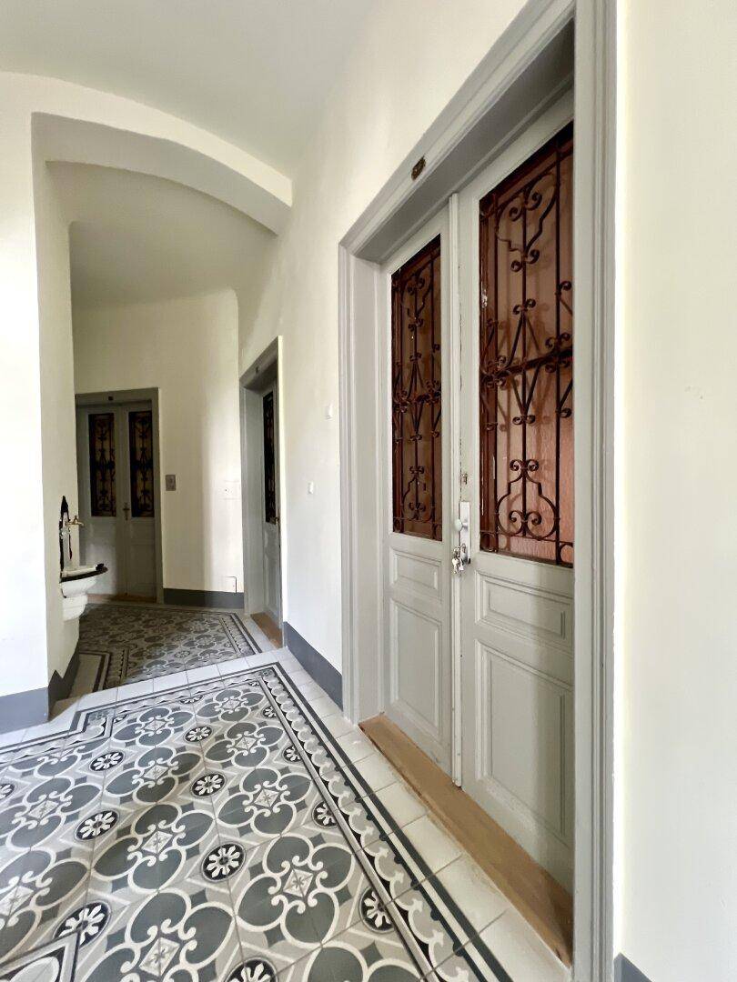 Heller Flur mit historischen Fliesen, hohen Decken und verzierten Doppeltüren im Altbau.