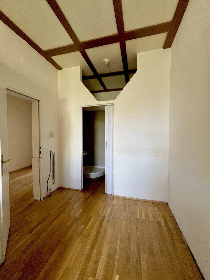 Flur mit Parkettboden und Holzbalkendecke, führt zu einem Badezimmer.