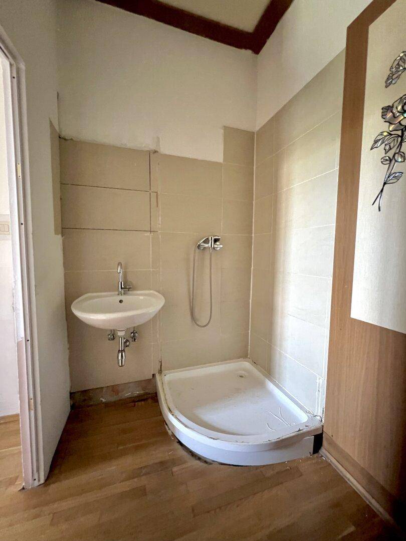 Einfaches Badezimmer mit Duschwanne und Waschbecken, bereit zur Renovierung.