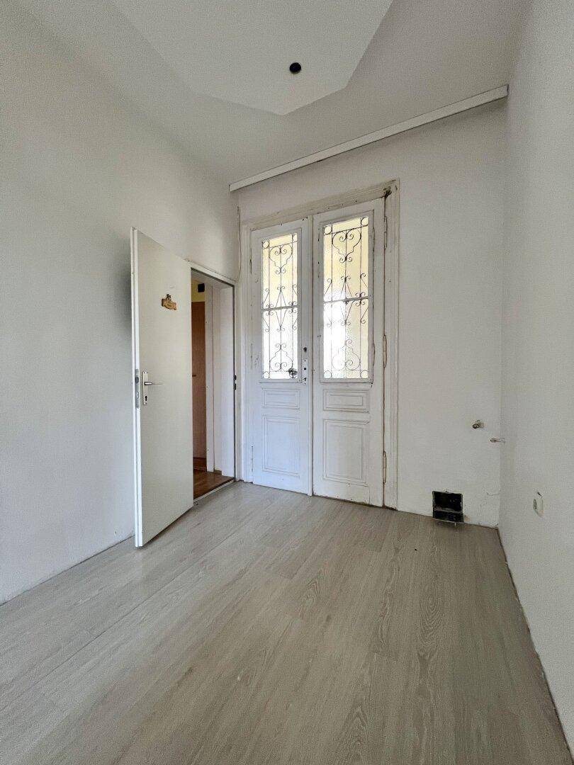 Leerer Raum mit hellem Laminatboden und doppelten Flügeltüren, möglicherweise mit Balkonzugang.