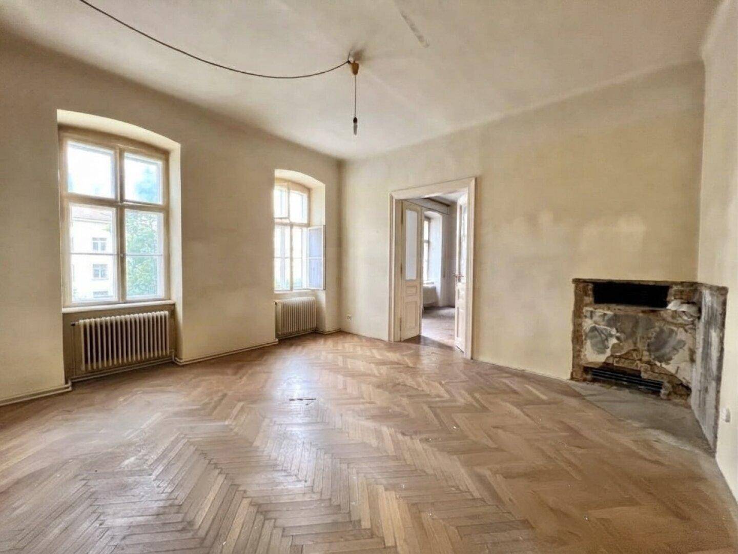 Geräumiges Zimmer mit Fischgrätparkett und einem renovierungsbedürftigen Kamin.
