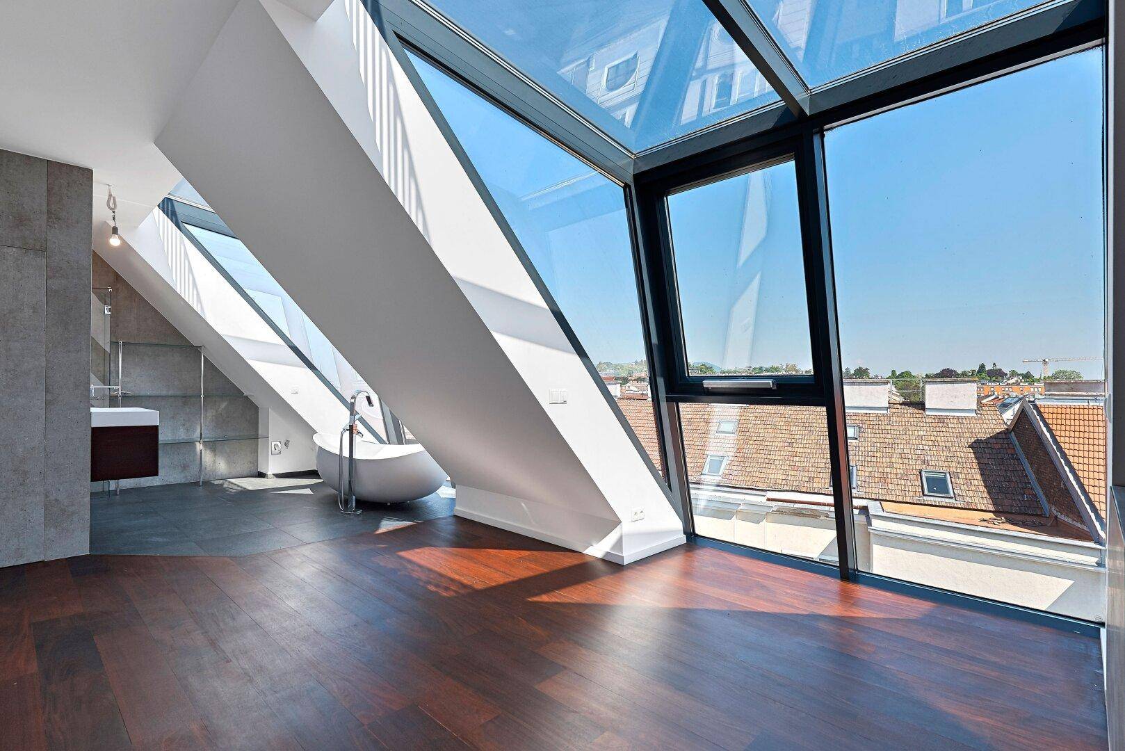 Modernes Badezimmer im Dachgeschoss mit freistehender Badewanne, großen Glasflächen und Blick über die Dächer.