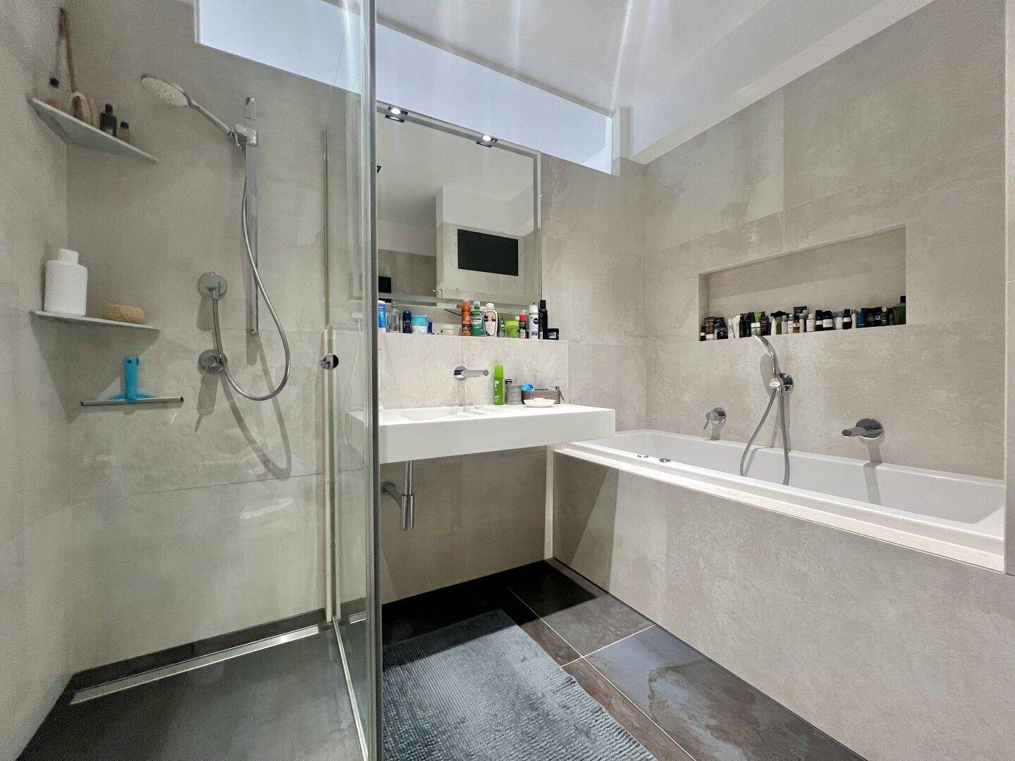 Modernes Badezimmer mit begehbarer Dusche, Badewanne und großformatigen Fliesen.