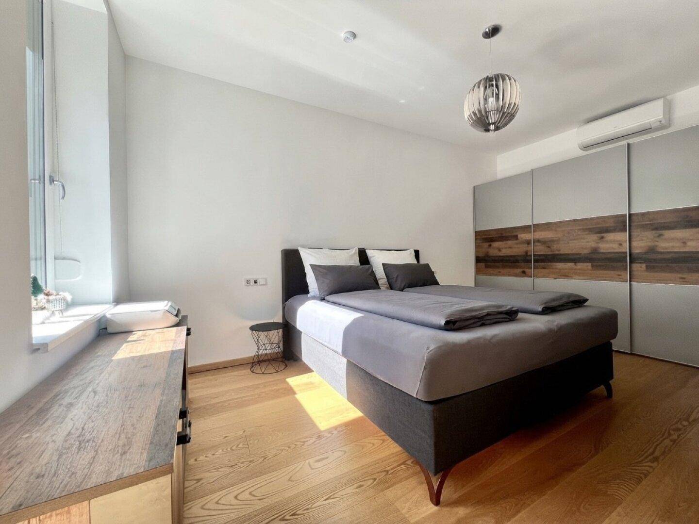 Helles Schlafzimmer mit Doppelbett, Holzboden, großem Kleiderschrank und Klimaanlage.