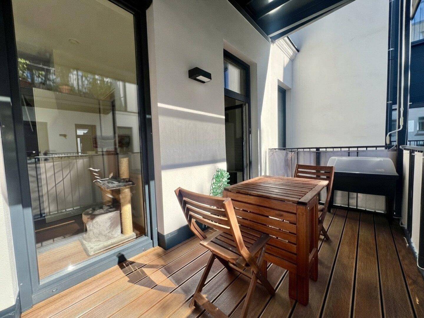 Sonniger Balkon mit Holzboden und Sitzgelegenheiten, direkt zugänglich vom Innenraum.