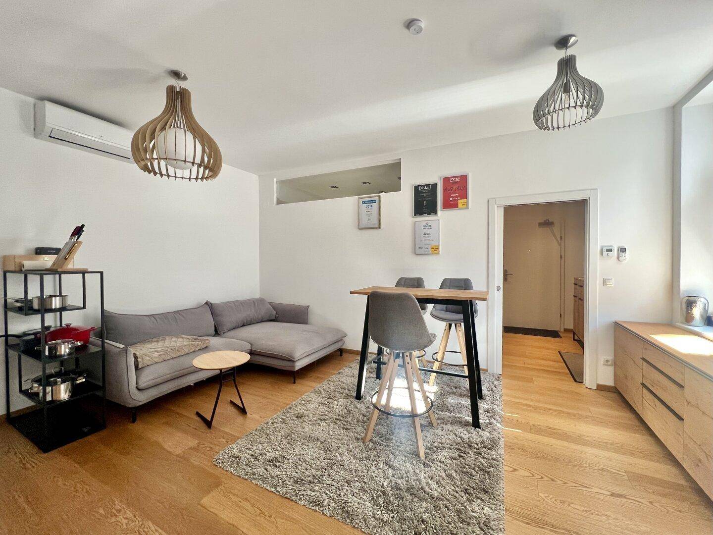 Heller Wohnbereich mit Sofa, Bartisch und modernem Regal, ausgestattet mit Klimaanlage.