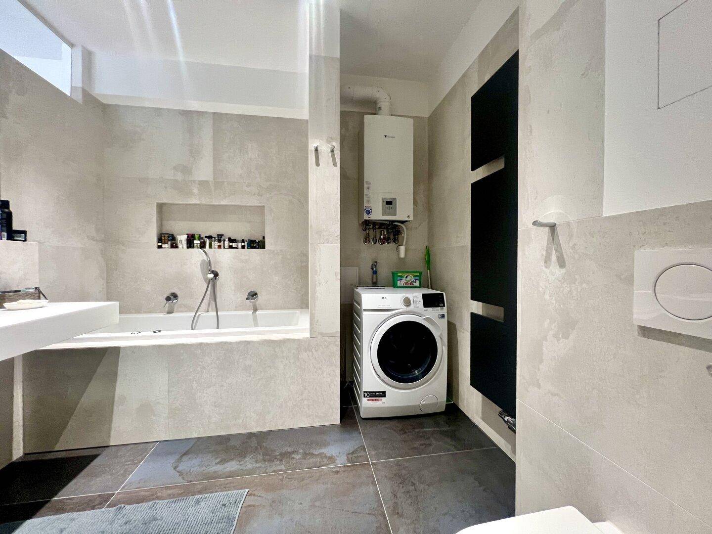 Badezimmer mit Badewanne, Waschmaschine, Warmwasserbereiter und beheiztem Handtuchhalter.