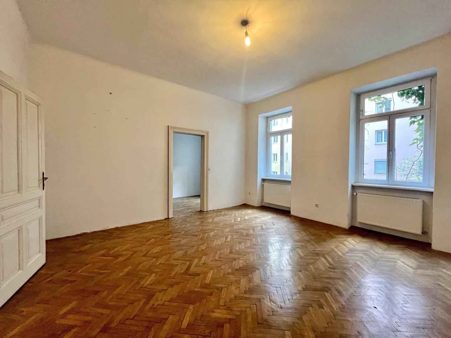 Geräumiges Zimmer mit Fischgrätparkett und hohen Decken, ideal für Wohn- oder Schlafbereich.