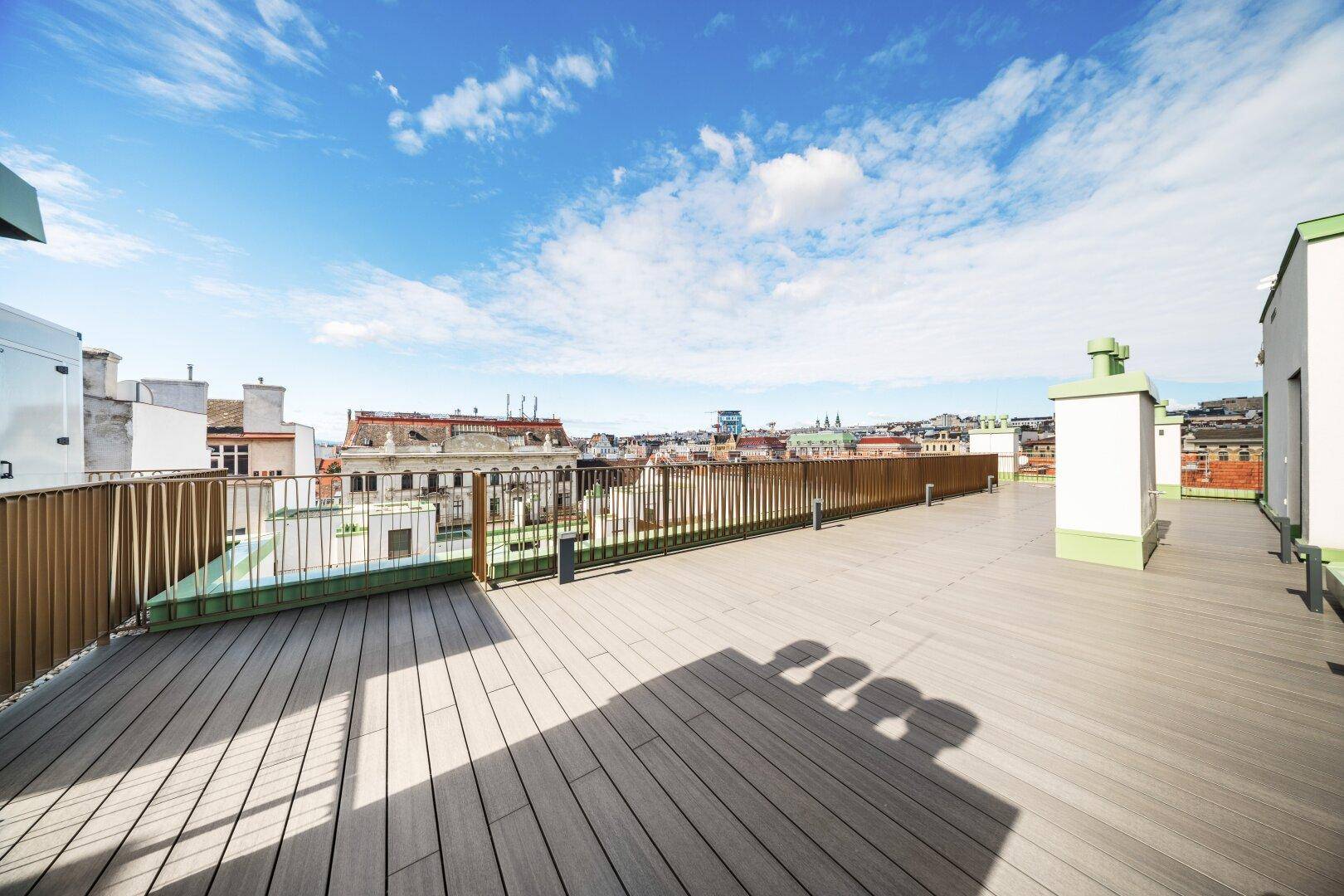 Große Dachterrasse mit Holzbelag und Panoramablick über die Stadt unter blauem Himmel.