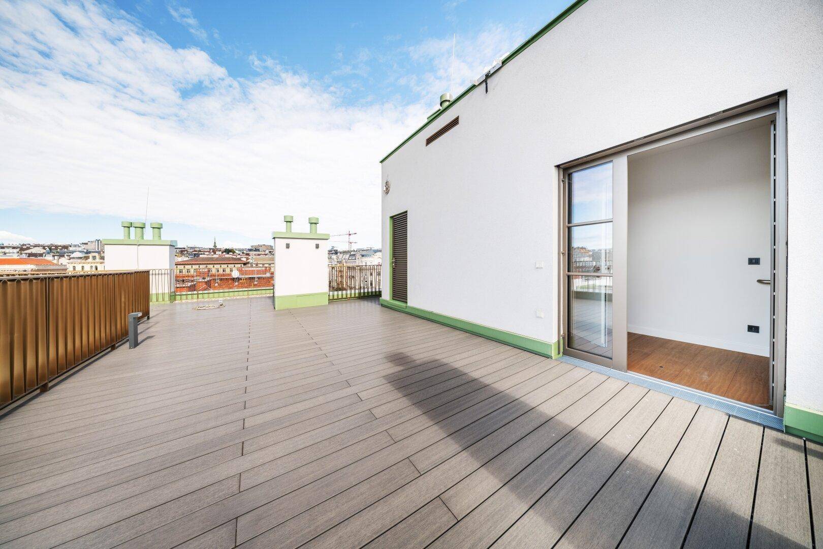 Geräumige Dachterrasse mit Holzboden und Zugang zu einem hellen Innenraum, mit Stadtblick.