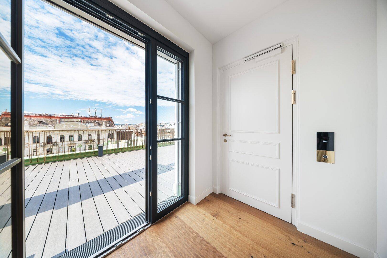 Heller Flur mit Holzboden und großer Schiebetür, die auf die sonnige Dachterrasse führt.