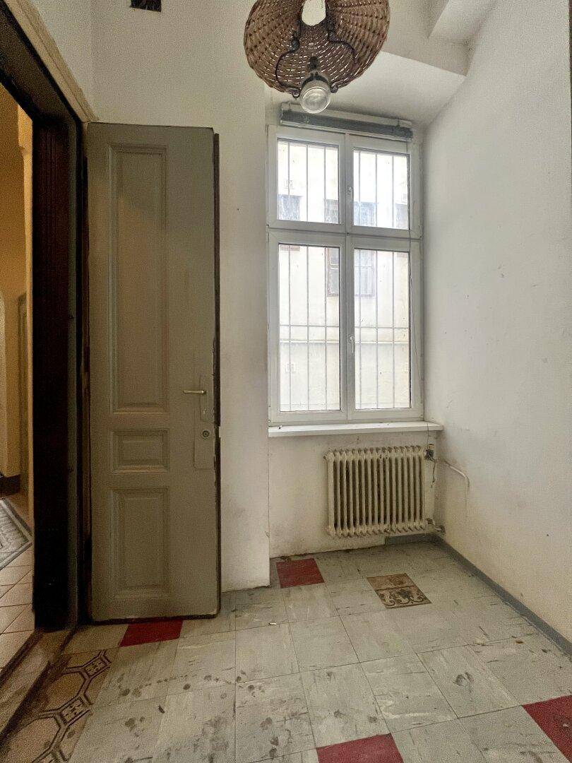Kleiner Eingangsbereich mit Fliesenboden, Fenster mit Gitter und Heizkörper.