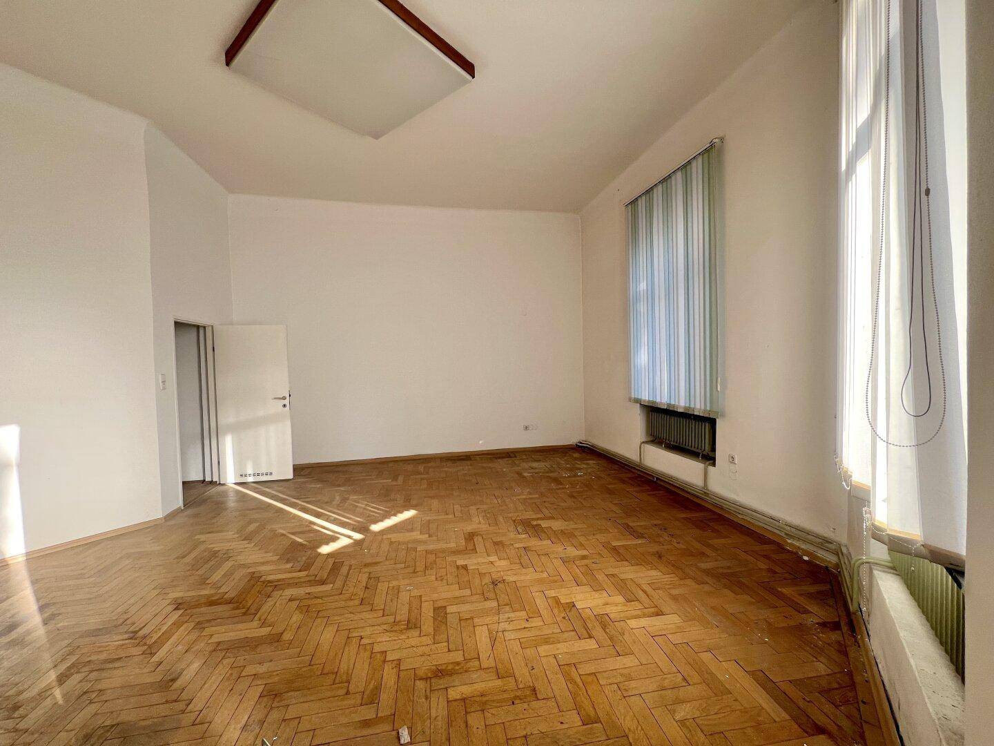 Geräumiges Zimmer mit Fischgrätparkett, hohen Decken und viel Tageslicht.