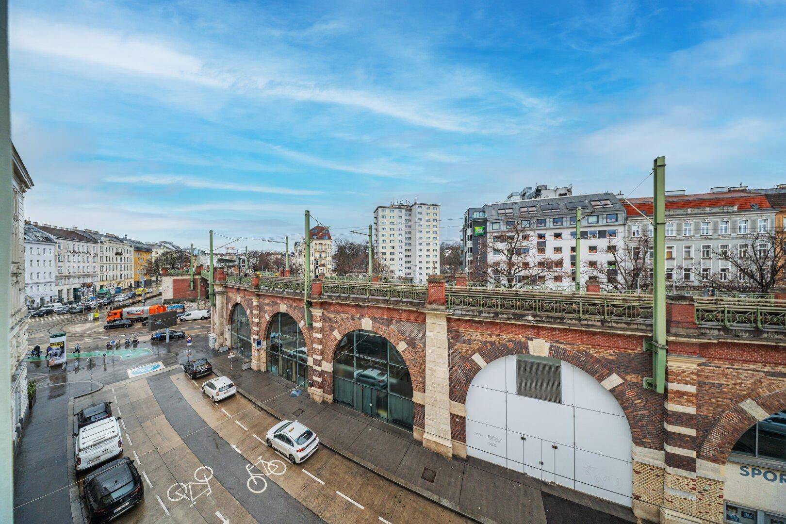 Weitläufiger Stadtblick mit historischer Eisenbahnbrücke und umliegenden Gebäuden unter blauem Himmel.