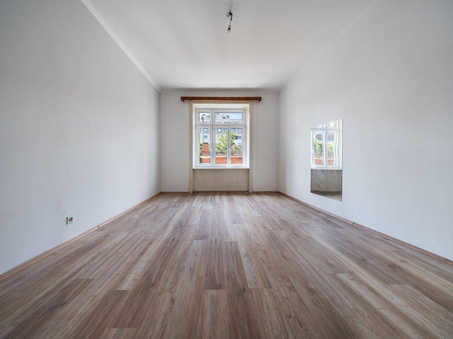 Geräumiges Zimmer mit Laminatboden und großem Fenster, das viel Tageslicht hereinlässt.