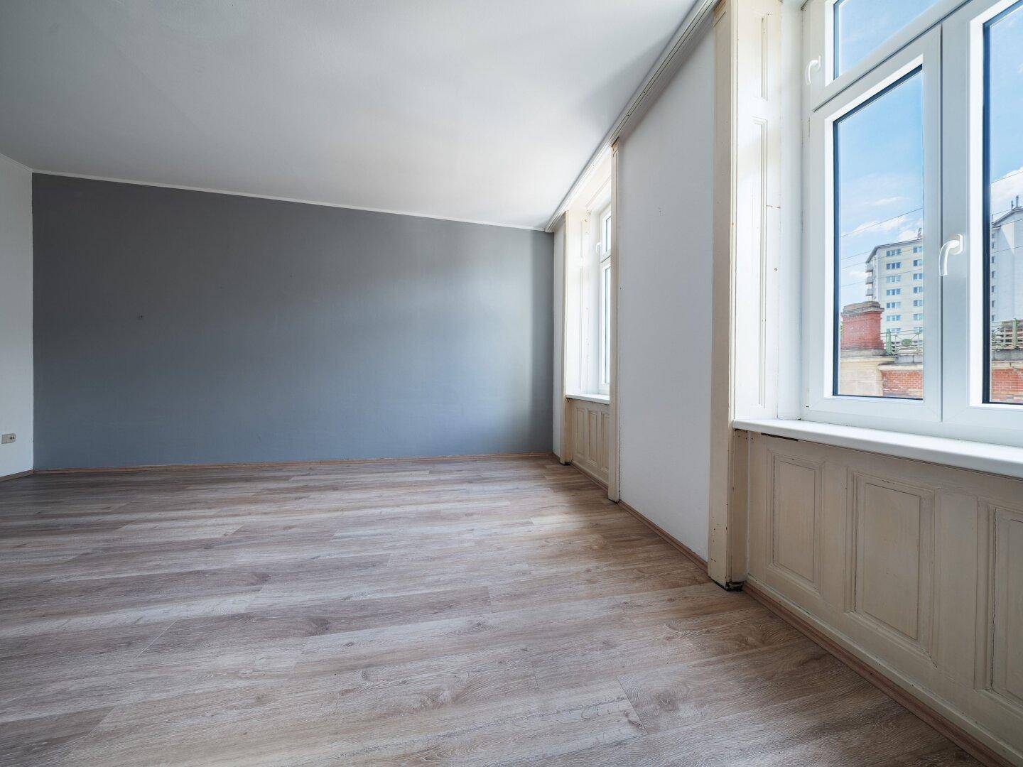 Helles Zimmer mit Laminatboden und einer grauen Akzentwand, ideal für ein Wohnzimmer.