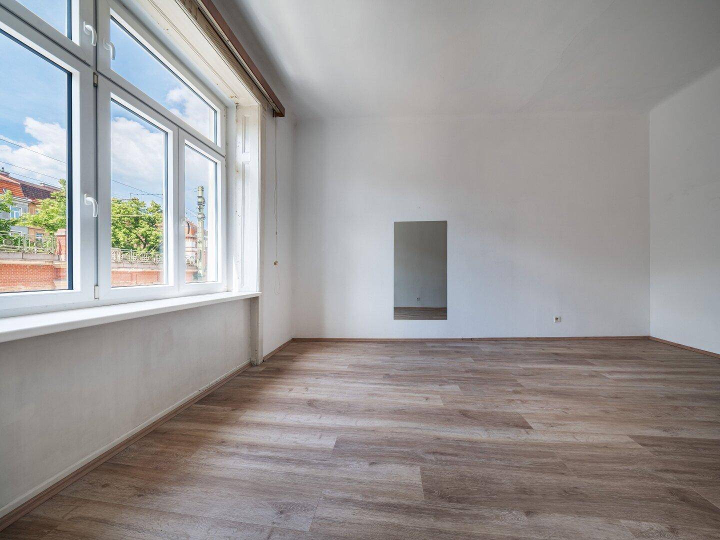 Helles Zimmer mit Laminatboden und großem Fenster, das einen Blick nach draußen bietet.