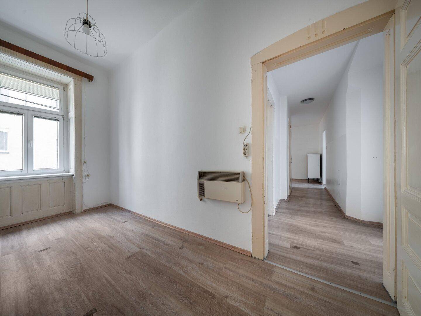 Helles Zimmer mit Laminatboden und Zugang zu einem Flur, ausgestattet mit einem Heizkörper.