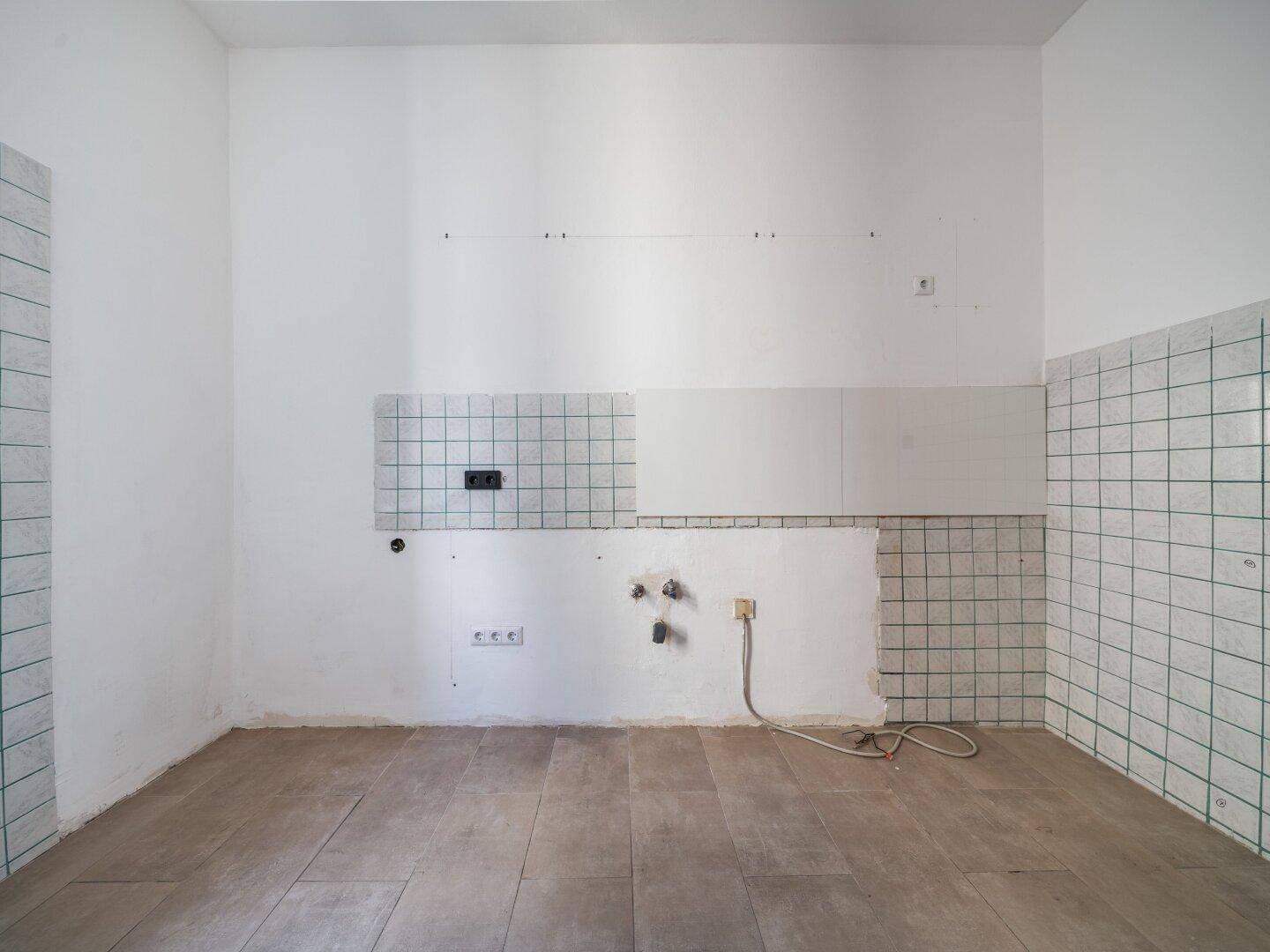 Leere Küche mit Fliesenboden und gefliesten Wänden, bereit für die Installation einer neuen Küchenzeile.