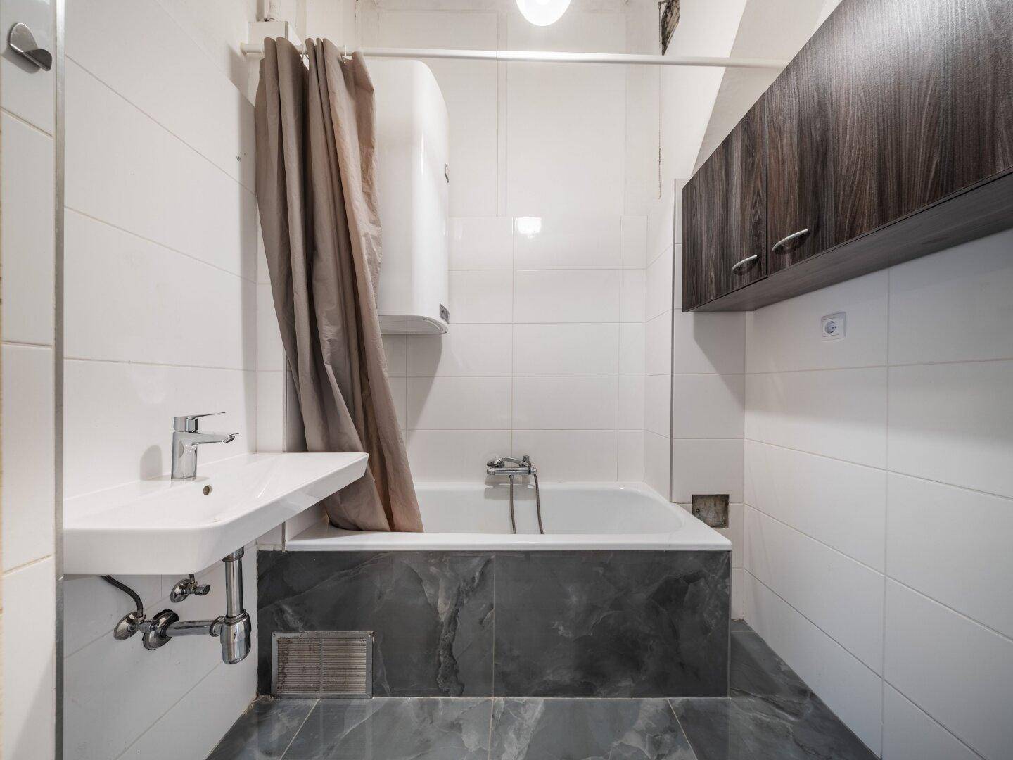 Modernes Badezimmer mit Badewanne, Waschbecken und weißen Fliesen, ausgestattet mit einem Boiler.