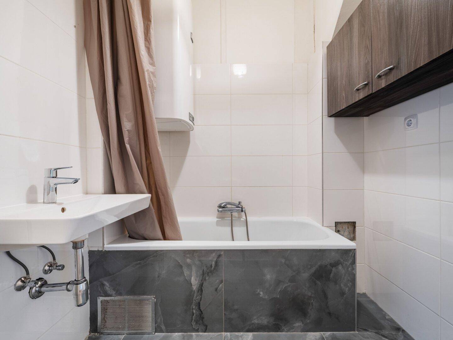 Helles Badezimmer mit Badewanne, Waschbecken und weißen Fliesen, bereit zur Nutzung.