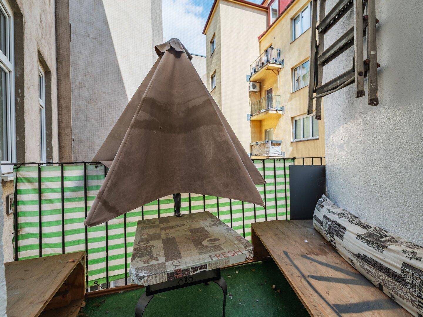 Kleiner Balkon mit Sonnenschirm und Sitzgelegenheiten, ideal für entspannte Stunden im Freien.