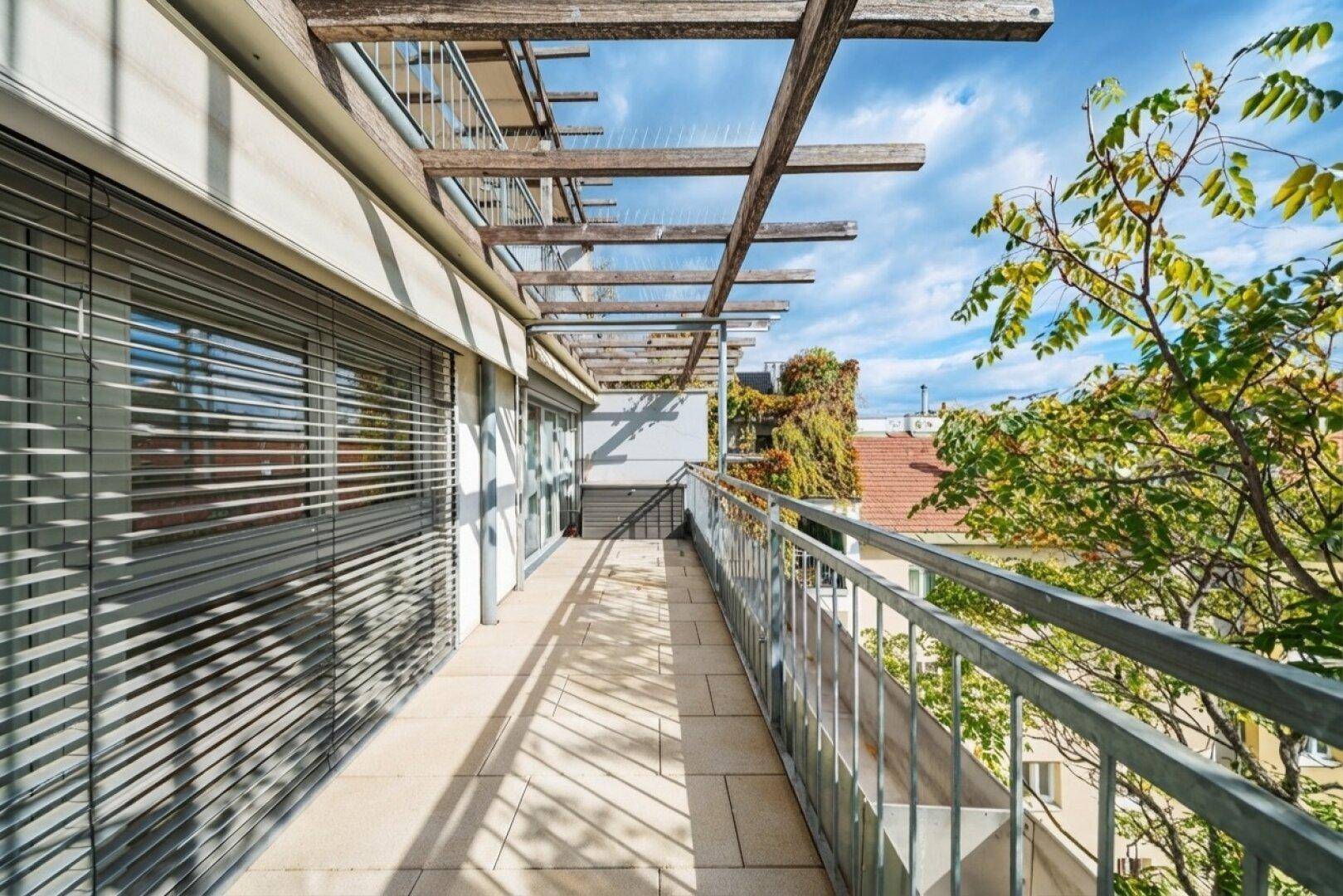 Langer Balkon mit Fliesenboden, Metallgeländer und Blick ins Grüne.