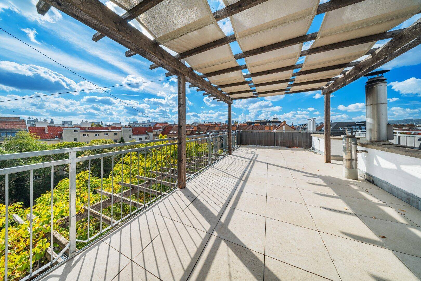 Geräumige Dachterrasse mit Pergola, Fliesenboden und Blick auf die Umgebung.