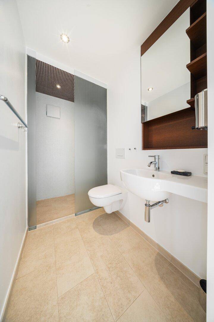 Modernes Badezimmer mit begehbarer Dusche, Wand-WC und elegantem Waschbecken auf Fliesenboden.