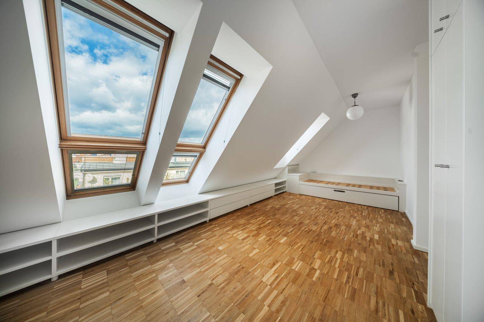 Geräumiges Schlafzimmer im Dachgeschoss mit mehreren Dachfenstern und Parkettboden.