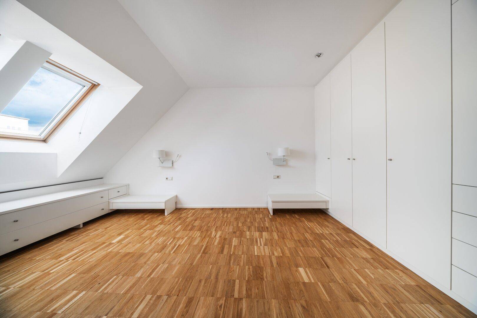 Helles Schlafzimmer im Dachgeschoss mit Einbauschränken, Dachfenster und Parkettboden.
