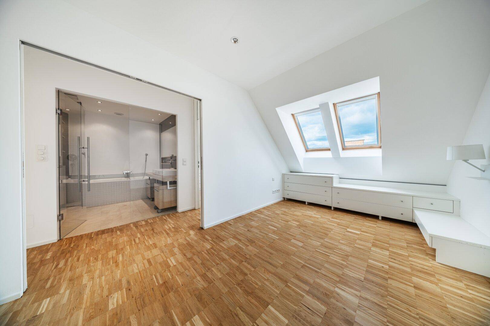 Schlafzimmer im Dachgeschoss mit Parkettboden, Dachfenstern und angrenzendem Badezimmer.