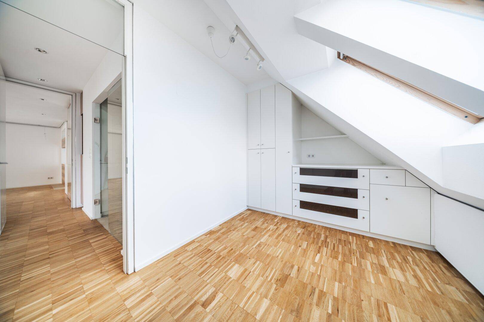 Dachgeschosszimmer mit Parkettboden, Dachfenster und praktischen Einbauschränken.