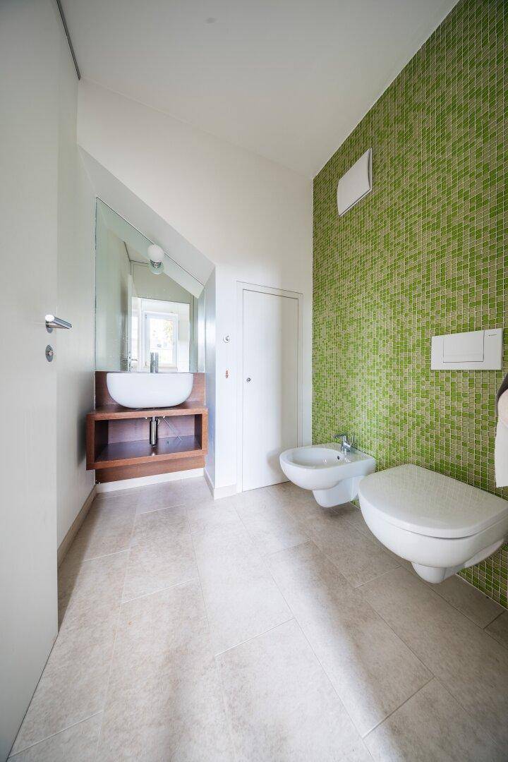 Modernes Badezimmer mit grünen Mosaikfliesen, Bidet und einem stilvollen Aufsatzwaschbecken.