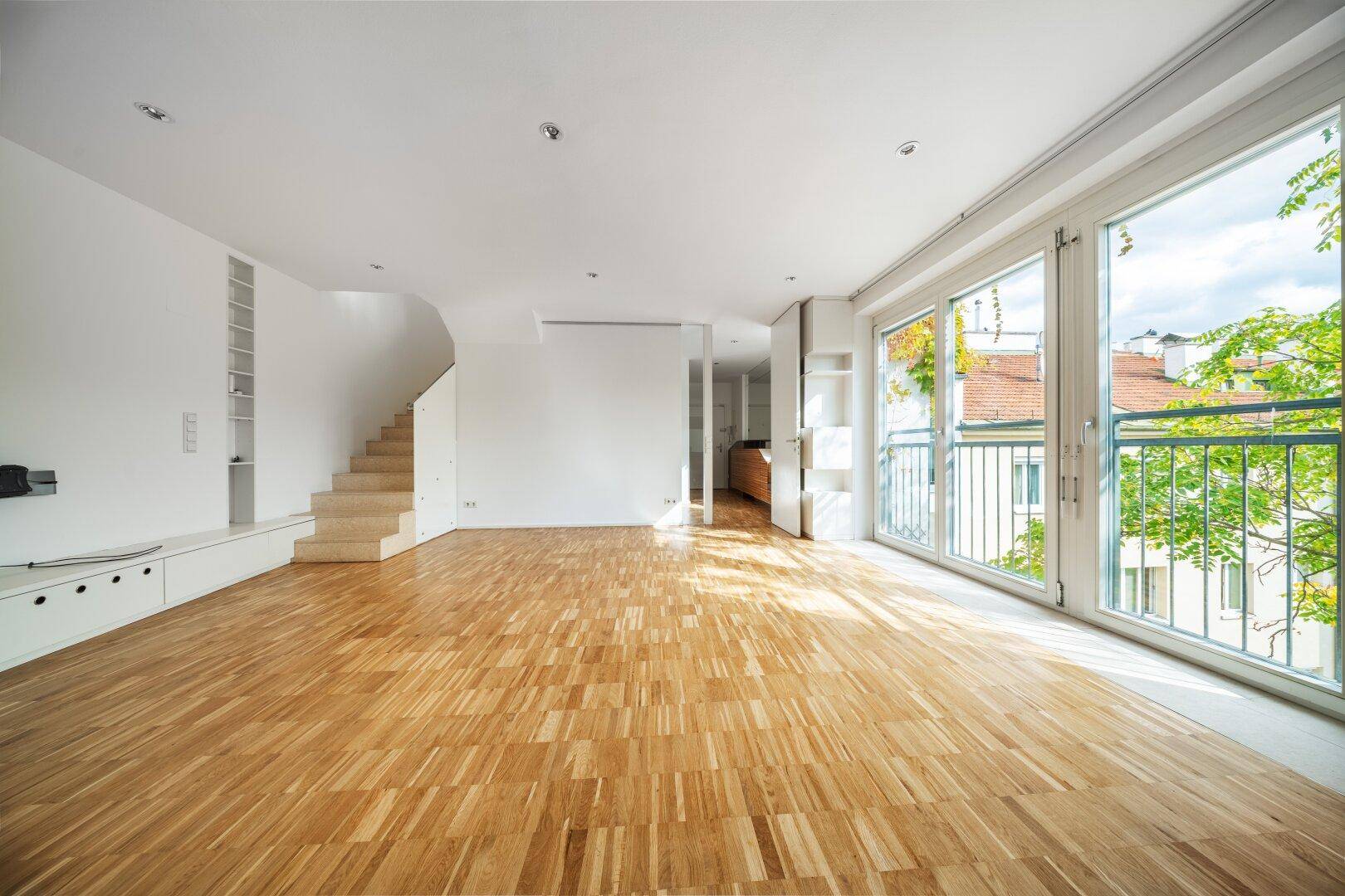 Helles Wohnzimmer mit Parkettboden, großen Fenstern und Zugang zu einem französischen Balkon.