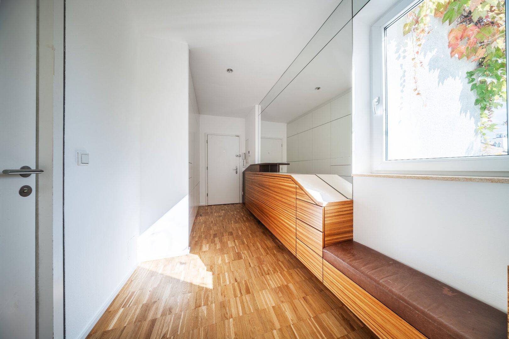 Eingangsbereich mit Holzboden, integrierter Sitzbank und einem Fenster, das Tageslicht hereinlässt.
