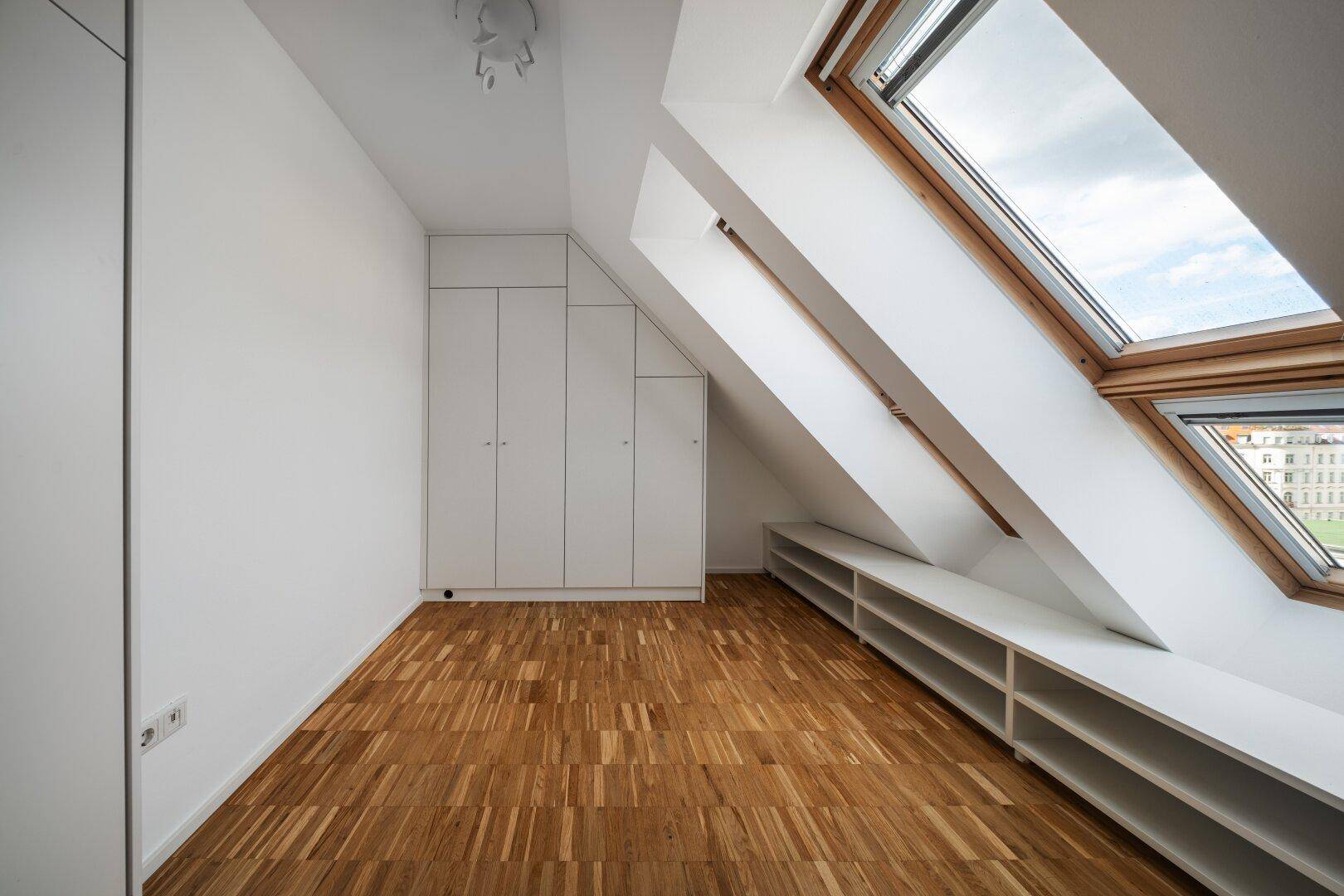 Dachgeschosszimmer mit Parkettboden, Dachfenstern und praktischen Einbauschränken.