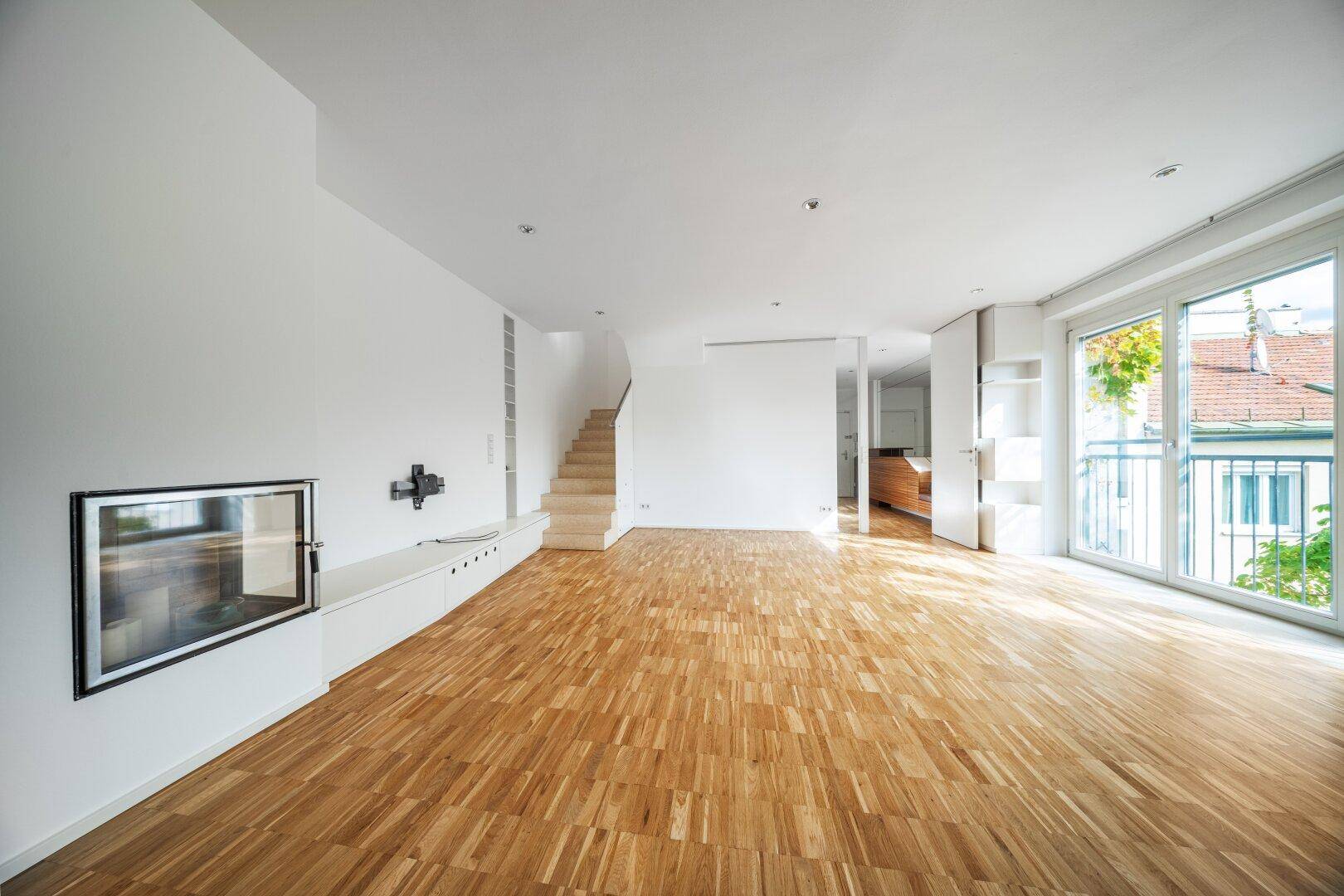 Geräumiger Wohnbereich mit Kamin, Parkettboden und Treppe zum oberen Stockwerk.