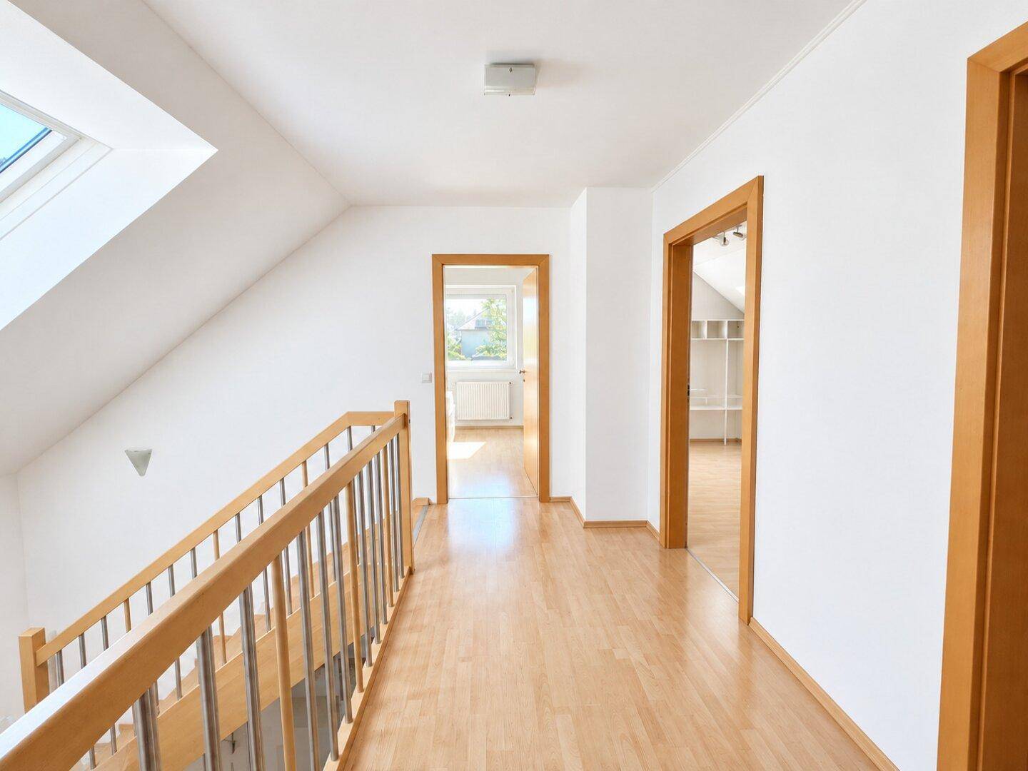 Heller Flur im Obergeschoss mit Holzboden, Holzgeländer und Dachfenster, das Tageslicht spendet.