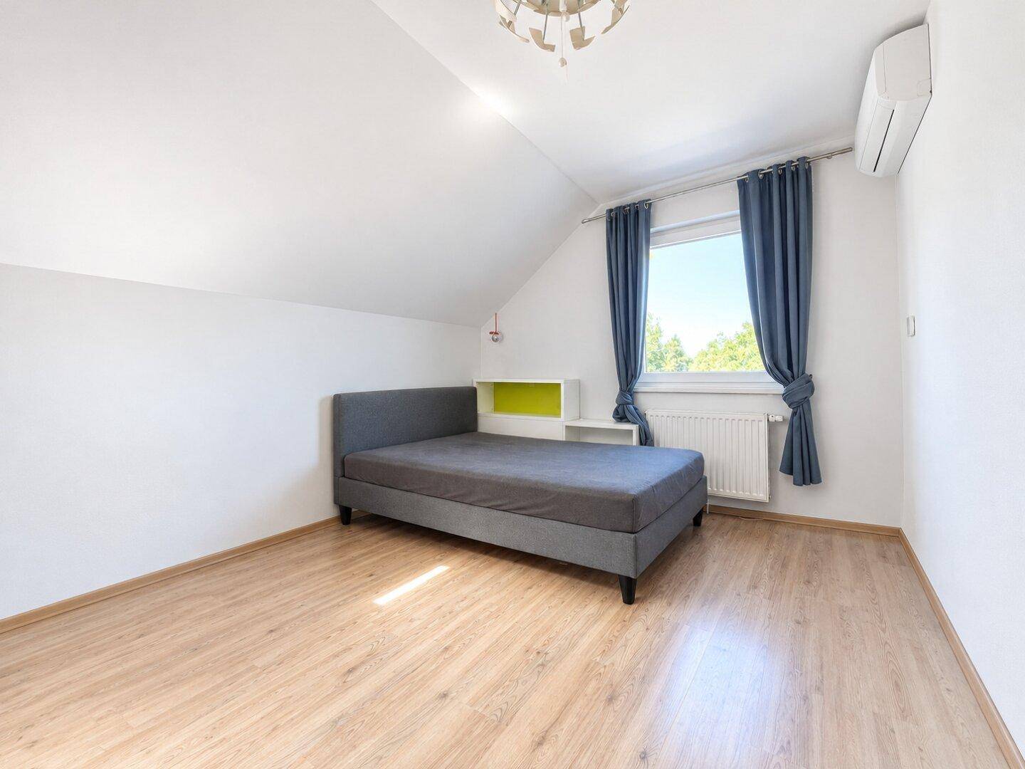 Gemütliches Schlafzimmer mit Holzboden, Einzelbett, Klimaanlage und Fenster mit blauen Vorhängen.