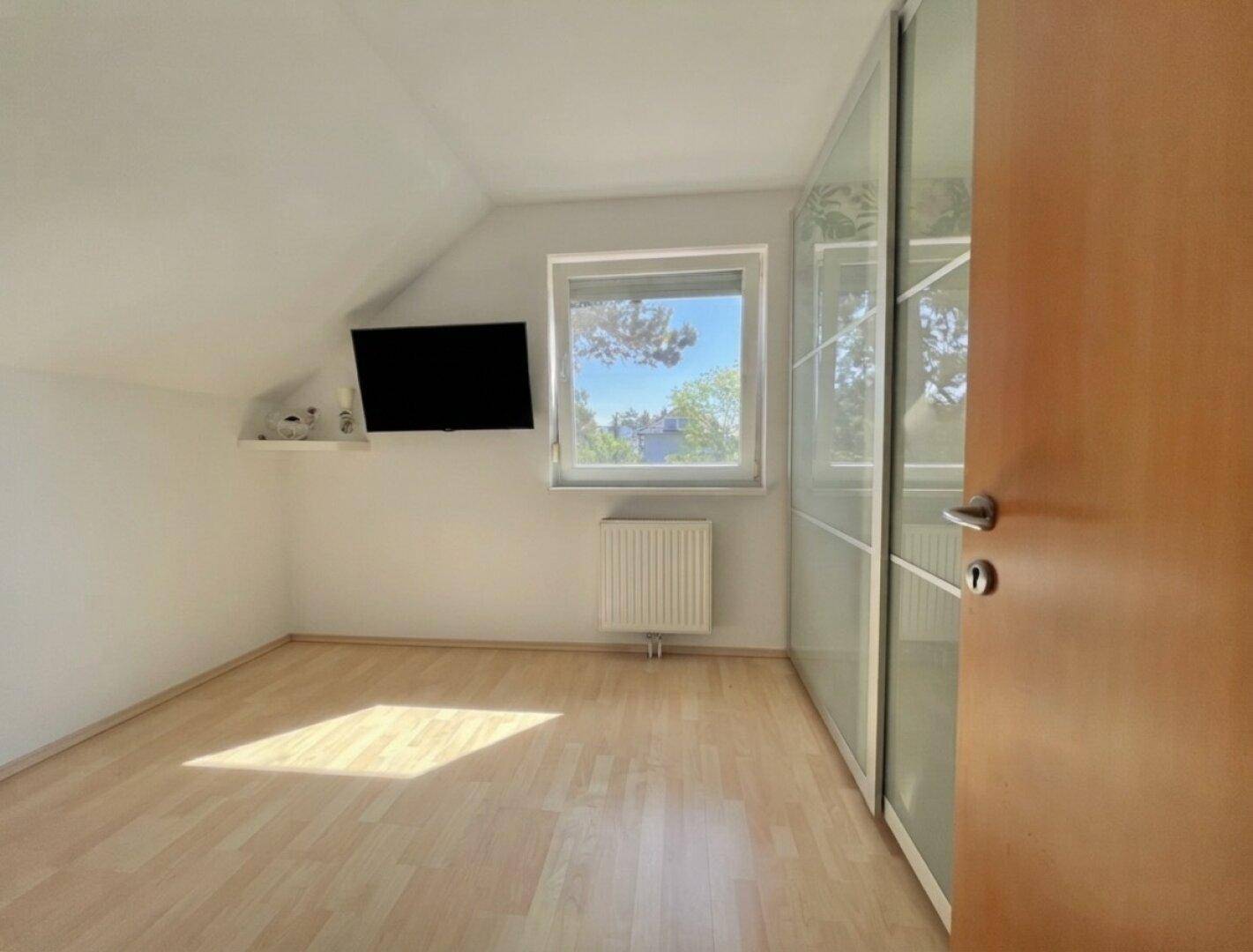 Helles Schlafzimmer mit Holzboden, Dachschräge und großem Einbauschrank mit Spiegeltüren.