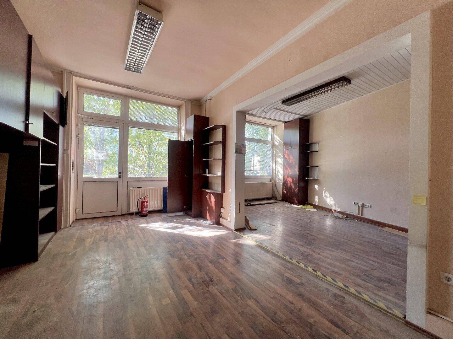 Geräumiger Innenraum mit Holzfußboden, großen Fenstern und integrierten Regalen.