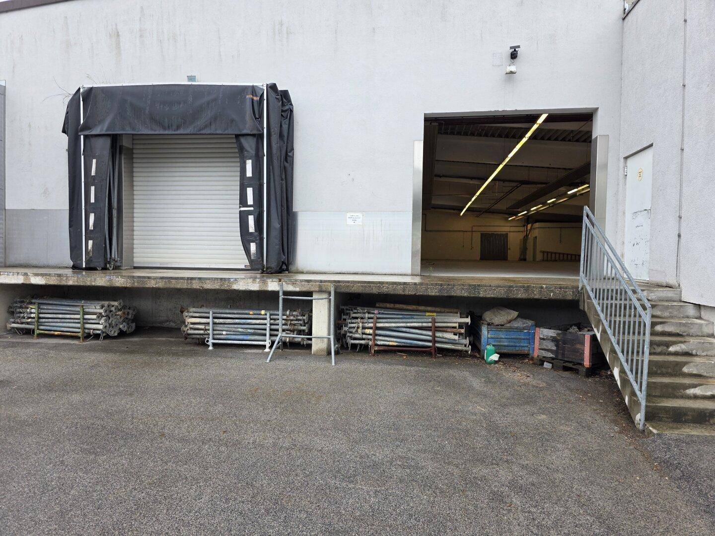 Außenansicht einer Laderampe mit Rolltor und Zugang zur Lagerhalle, umgeben von einer Zufahrt.