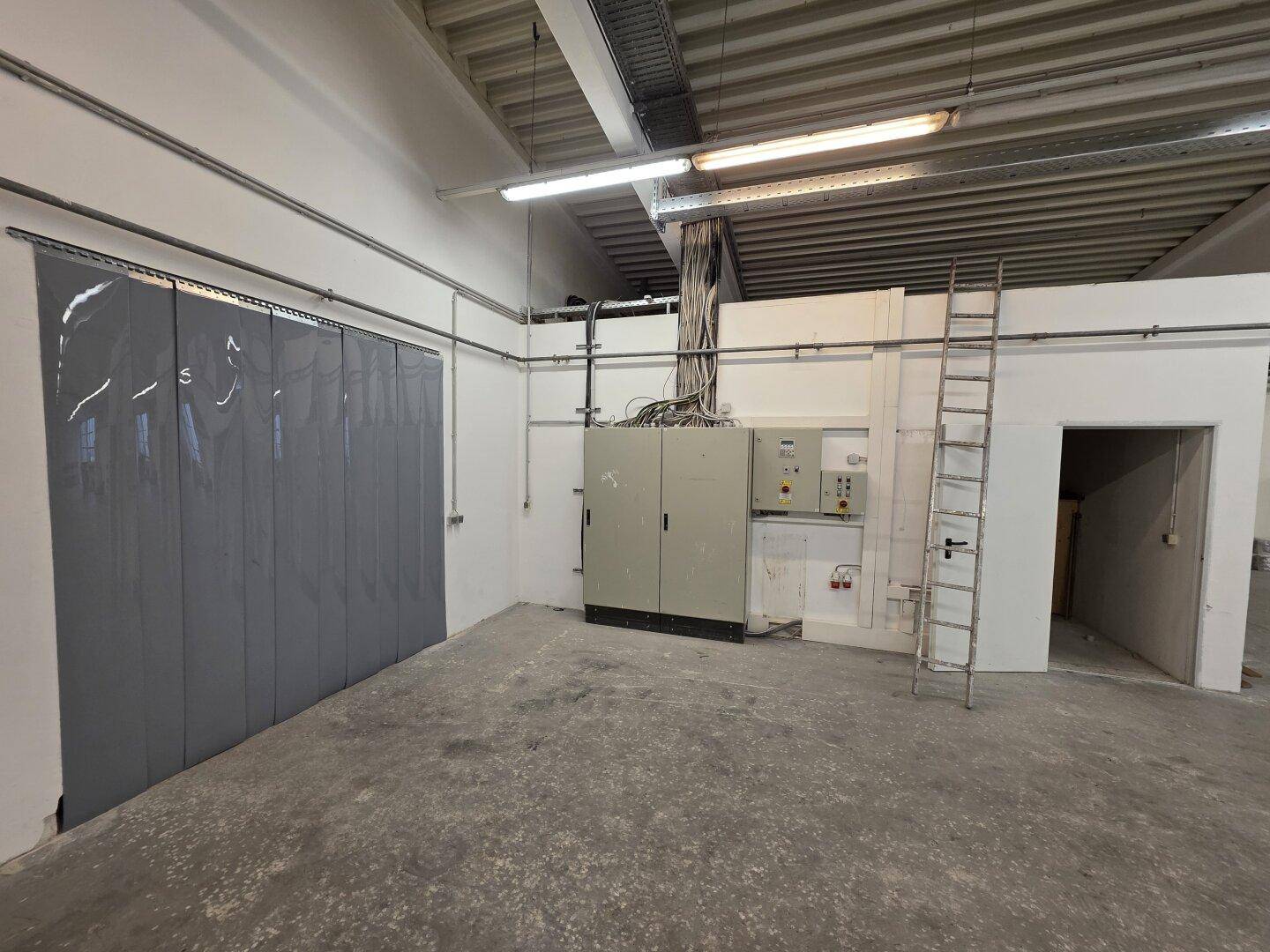 Bereich mit elektrischen Schaltschränken und Verkabelung in einer Ecke der Lagerhalle, mit Leiter.