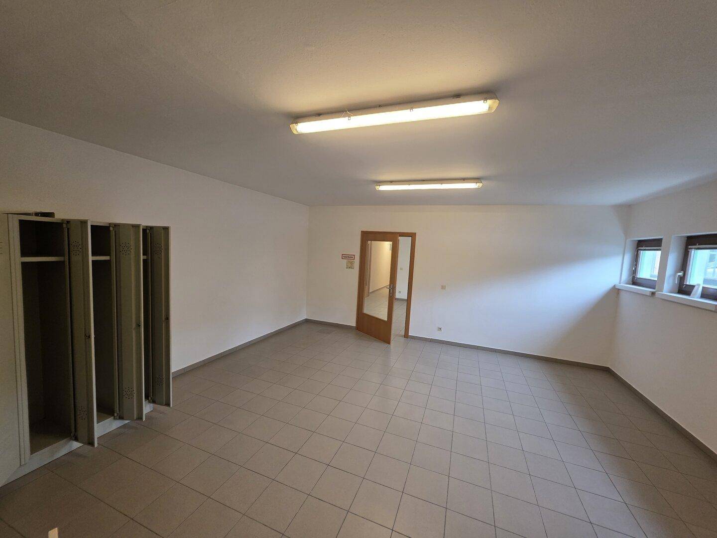 Heller Raum mit Fliesenboden und Spinden, geeignet als Büro oder Umkleidebereich, mit Fenster.