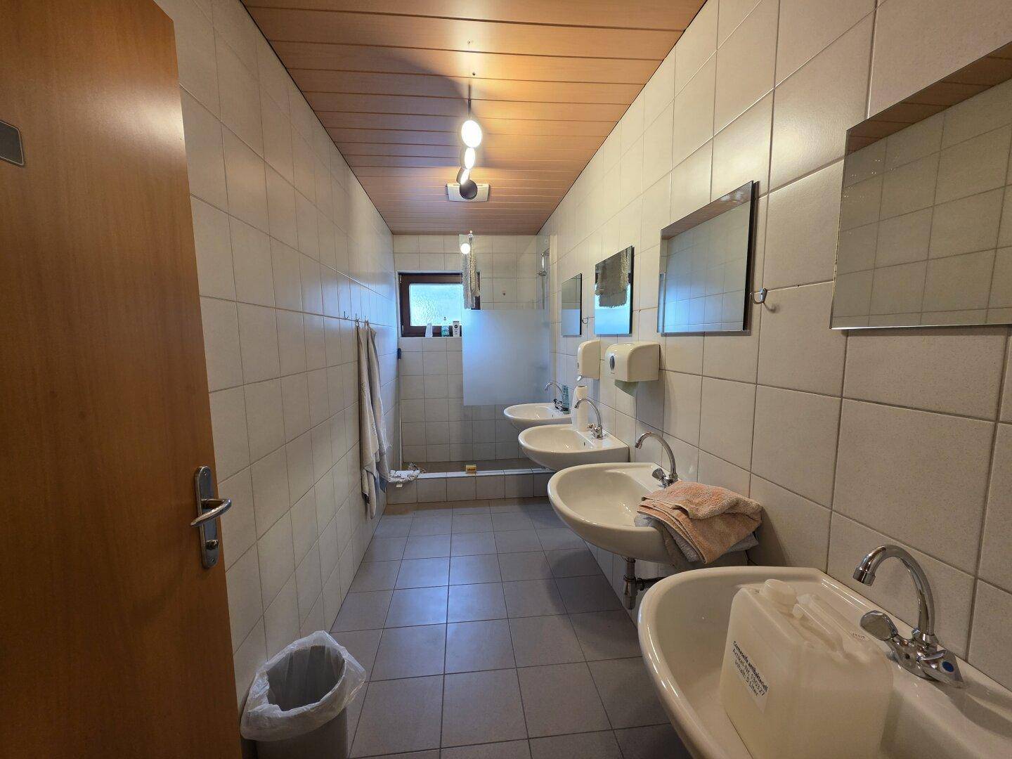 Waschraum mit mehreren Waschbecken, Fliesenwänden und Holzdecke, ideal für Mitarbeiter.