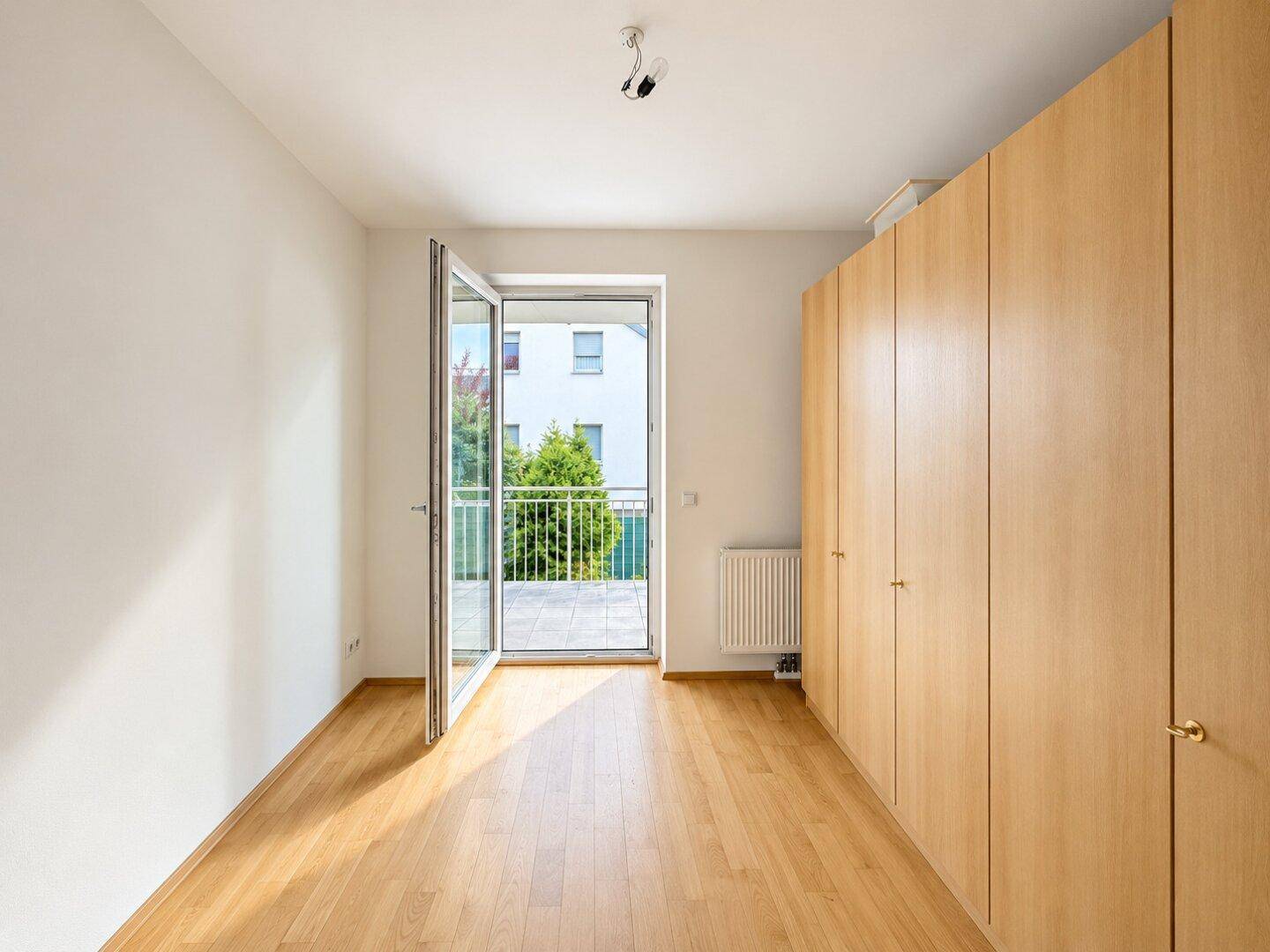 Helles Schlafzimmer mit Holzboden, Einbauschränken und direktem Zugang zum Balkon.