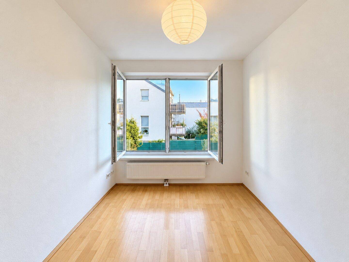 Helles Zimmer mit Holzboden, großem Fenster und Blick auf die Nachbarschaft.